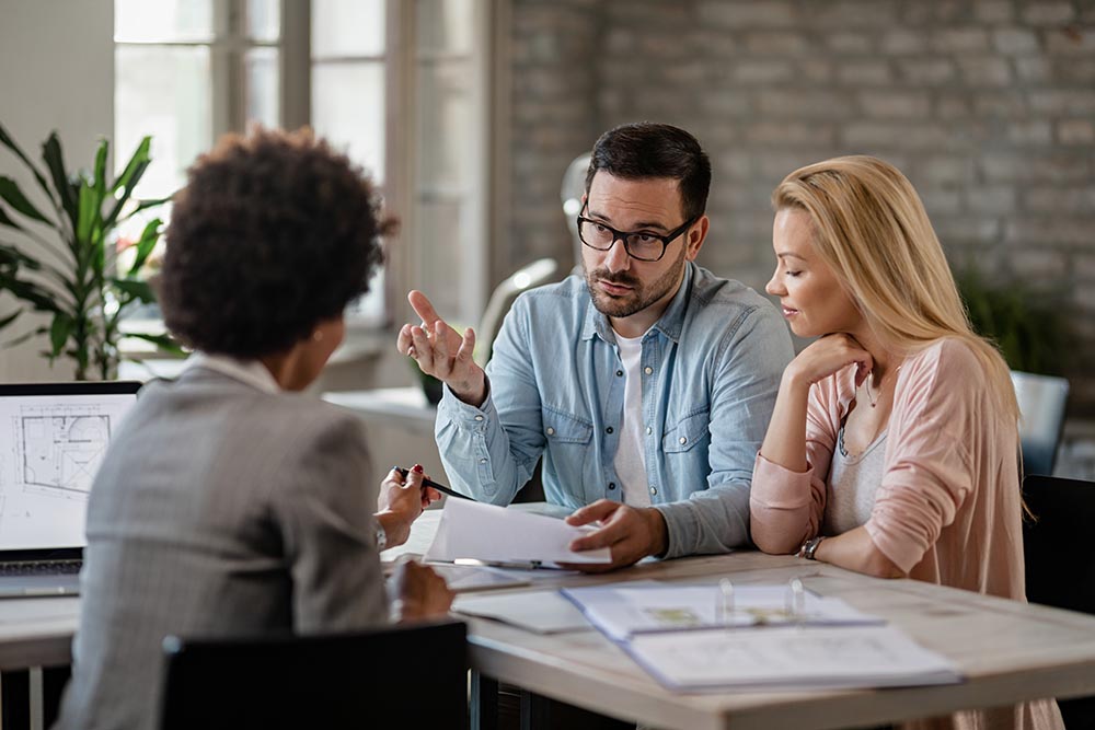 Mid adult couple discussing with financial advisor while analyzing documents on a meeting in the office.